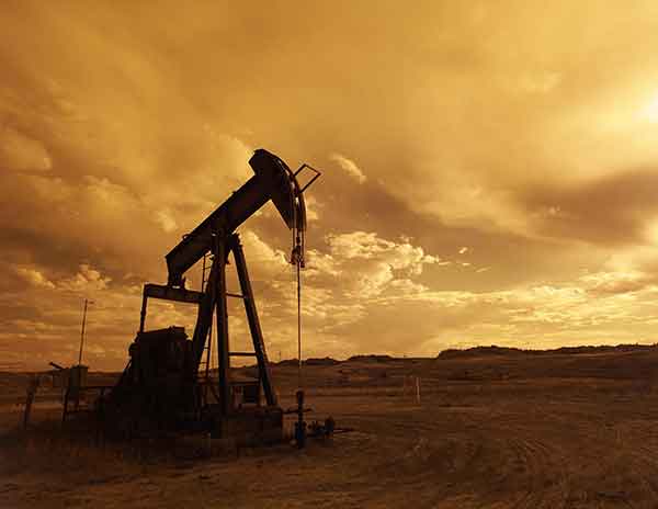 Oil pumpjack silhouette at sunset in desert landscape.