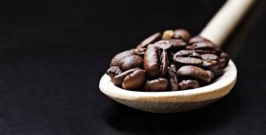 Roasted coffee beans on wooden spoon, dark background