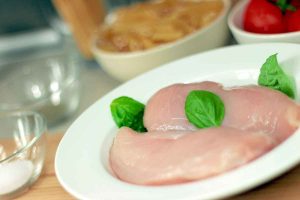 Raw chicken breasts with basil, tomatoes in background.
